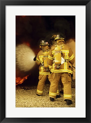 Framed Rear view of three firefighters extinguishing a fire Print