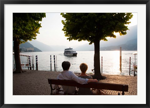 Framed Couple sitting on bench and watching ferry approaching dock along the Lake Como, Bellagio, Province of Como, Lombardy, Italy Print