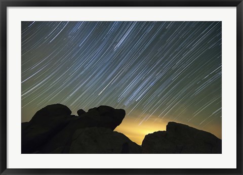 Framed Light pollution illuminates the sky and star tails above large boulders Print